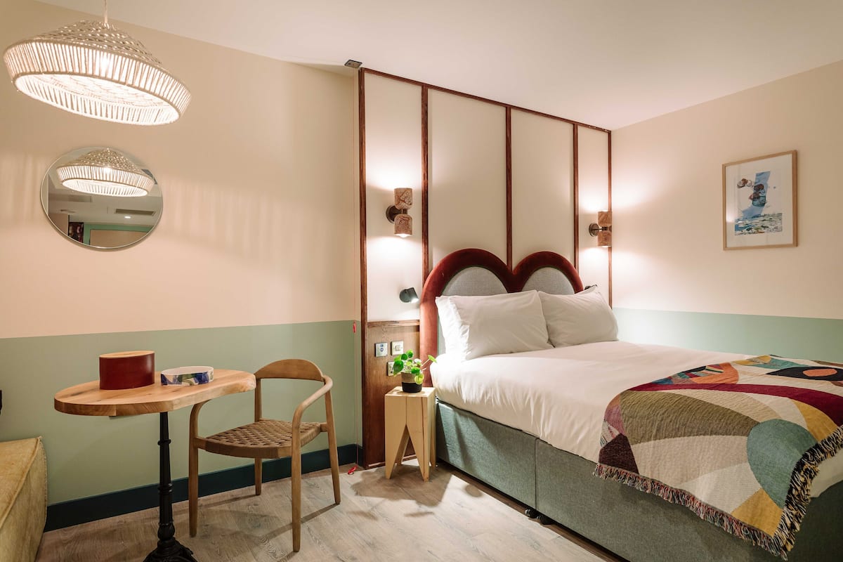 Un dormitorio con cama, mesita de noche, una silla, un espejo y una lámpara colgante.