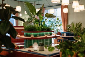 A restaurant interior with a green-tiled counter, hanging pendant lights, and various potted plants. - Second Nature Belfast (Belfast)