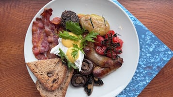 A plate of breakfast food including bacon, eggs, mushrooms, tomatoes, and toast on a wooden table.