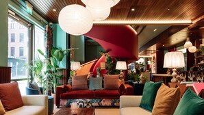 A modern hotel lobby with a red sofa, beige armchairs, and a wooden coffee table with books. - Second Nature Belfast (Belfast)