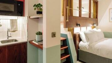 Habitación de hotel compacta con kitchenette, una cama, una mesita de noche y un espejo.