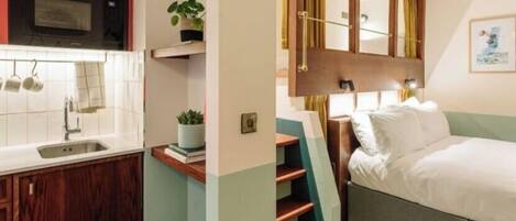 Een kleine hotelkamer met kitchenette, een bed, nachtkastje en spiegel.