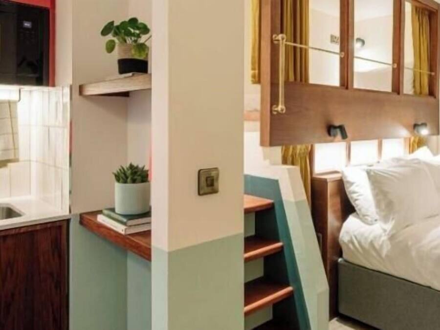 Habitación de hotel compacta con kitchenette, una cama, una mesita de noche y un espejo.