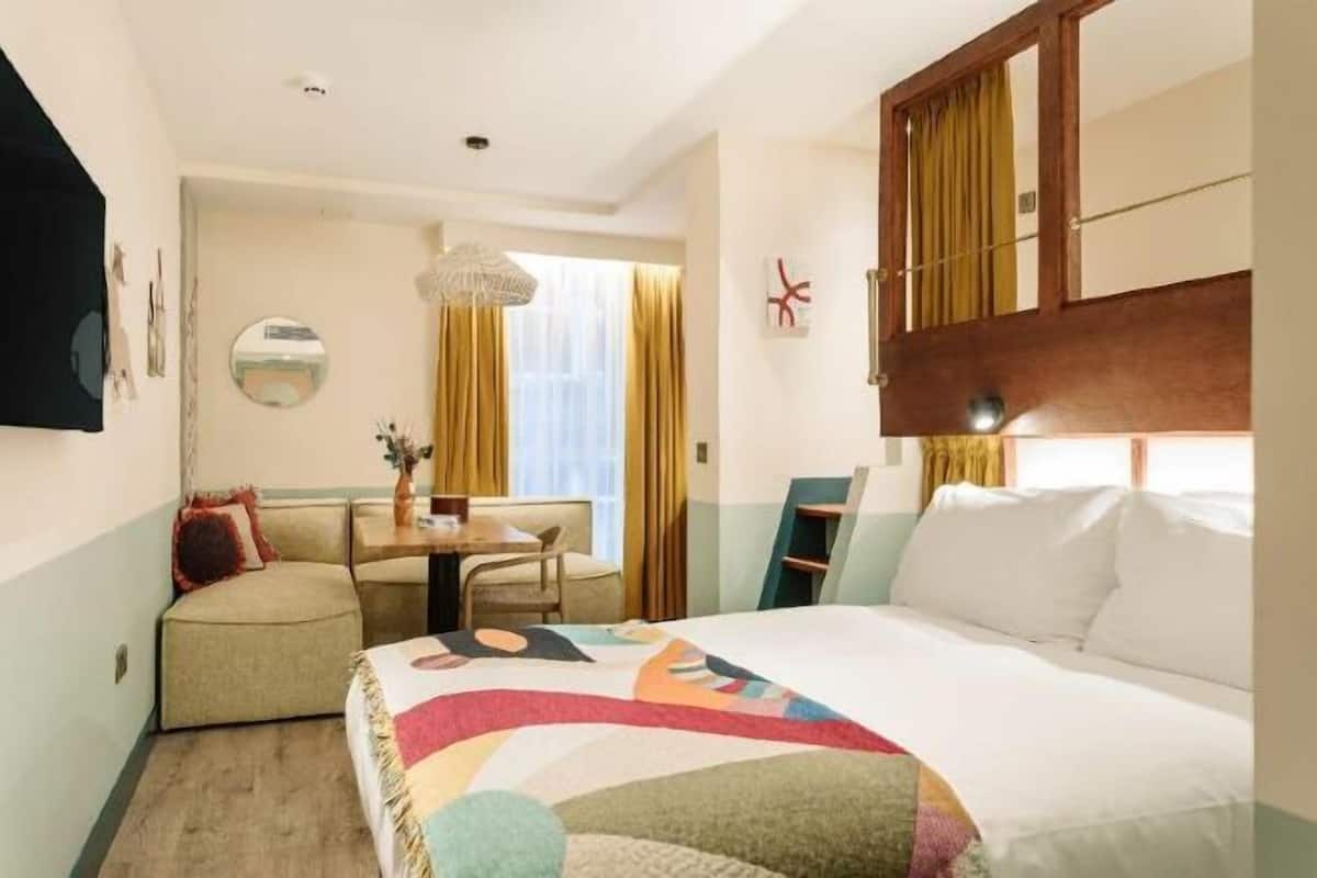 Habitación de hotel con cama, escritorio, silla, espejo y ventana con cortinas.