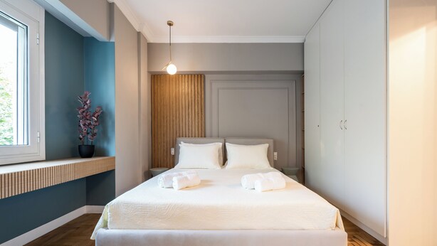 A modern bedroom with a large bed, a bedside table, a window, and a wooden panel wall.