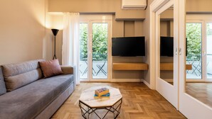 A modern living room with a sofa, a coffee table, a TV, and a balcony with outdoor furniture.