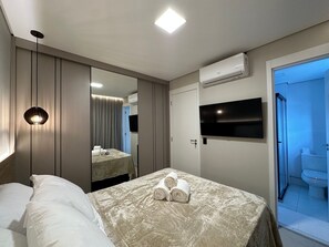 A hotel room with a bed, a bedside table, a mirror, a flat-screen TV, an air conditioning unit, and a bathroom visible through an open door. - Z Cotovia (São Paulo)