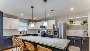 A modern kitchen with a central island, bar stools, stainless steel appliances, and pendant lighting. - Garden Peak in Central Dallas, TX (Dallas)
