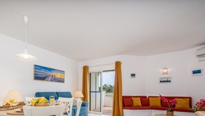 A bright living room with a dining area, a sofa, and a table set with fruits and drinks. - #174 T2 em Zona Tranquila by Home Holidays (Albufeira)