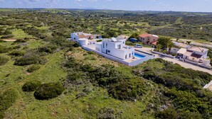 En modern villa med en swimmingpool, omgiven av frodig grönska och kullar.