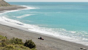 Uma praia com uma duna, uma pessoa em veículo off-road e o oceano.