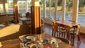 Uma sala de jantar com mesa de madeira posta para o café da manhã, cercada por grandes janelas com vista para o exterior.