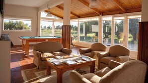 Uma sala de estar ampla com mesa de bilhar, assentos confortáveis e grandes janelas com vista para o exterior.