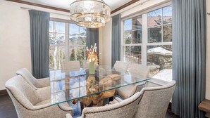 A dining area with a glass table, upholstered chairs, a chandelier, and a view through large windows. - Cassidy Ridge D101 Condo (Mountain Village)
