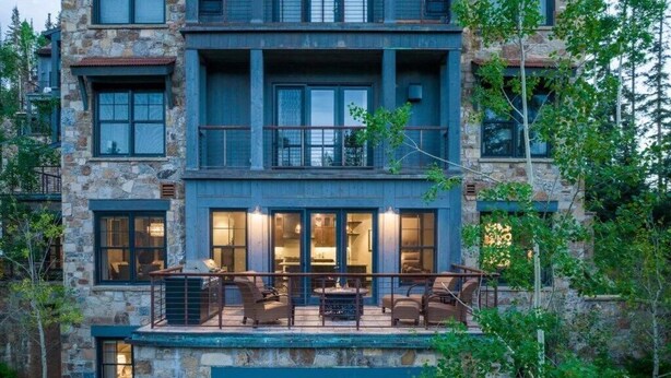 A multi-story stone building with balconies, large windows, and outdoor seating. - Luxury Mountain Village Retreat | Cassidy Ridge 4BR with Panoramic Views (Mountain Village)