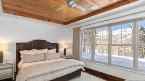 A bedroom with a large bed, wooden ceiling, and a window with a view of a snowy landscape. - Cassidy Ridge D101 Condo (Mountain Village)