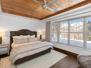 Une chambre avec un grand lit, un plafond en bois et une fenêtre donnant sur un paysage enneigé.