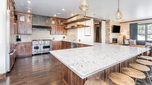 A spacious kitchen with a large island, wooden cabinets, and a stone accent wall. - Luxury Mountain Village Retreat | Cassidy Ridge 4BR with Panoramic Views (Mountain Village)