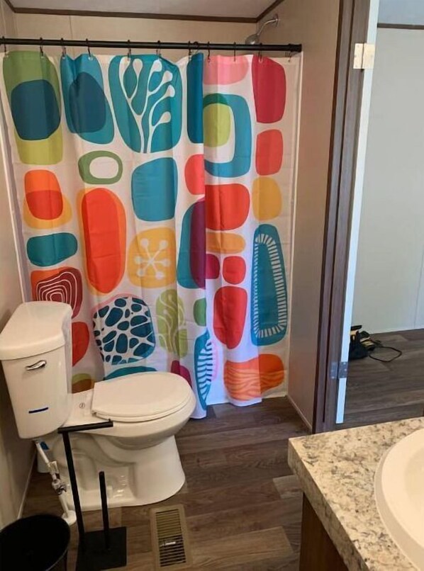 Ein Badezimmer mit einer weißen Toilette, einer Duschkabine mit farbenfrohen, abstrakten Mustern und einer Waschtischplatte aus Granit.
