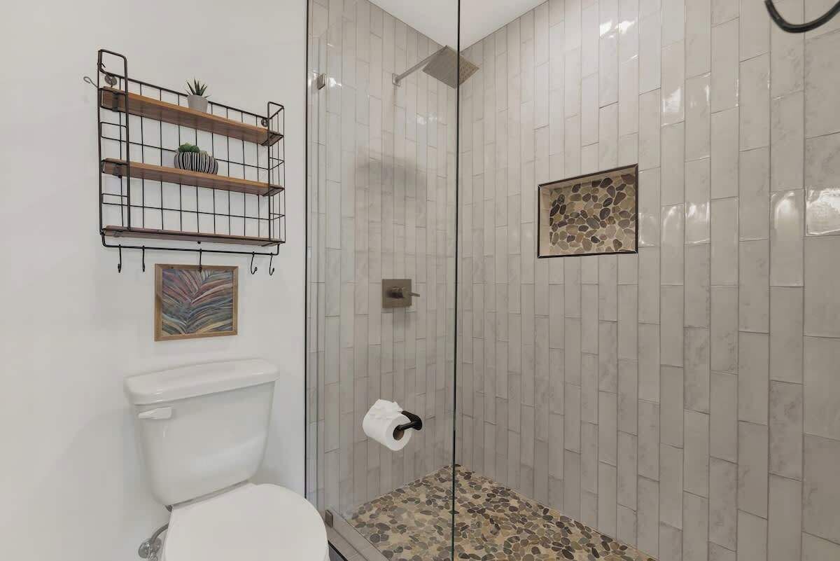 Een badkamer met een douchecabine van glas, een toilet en een plank met decoratieve objecten.