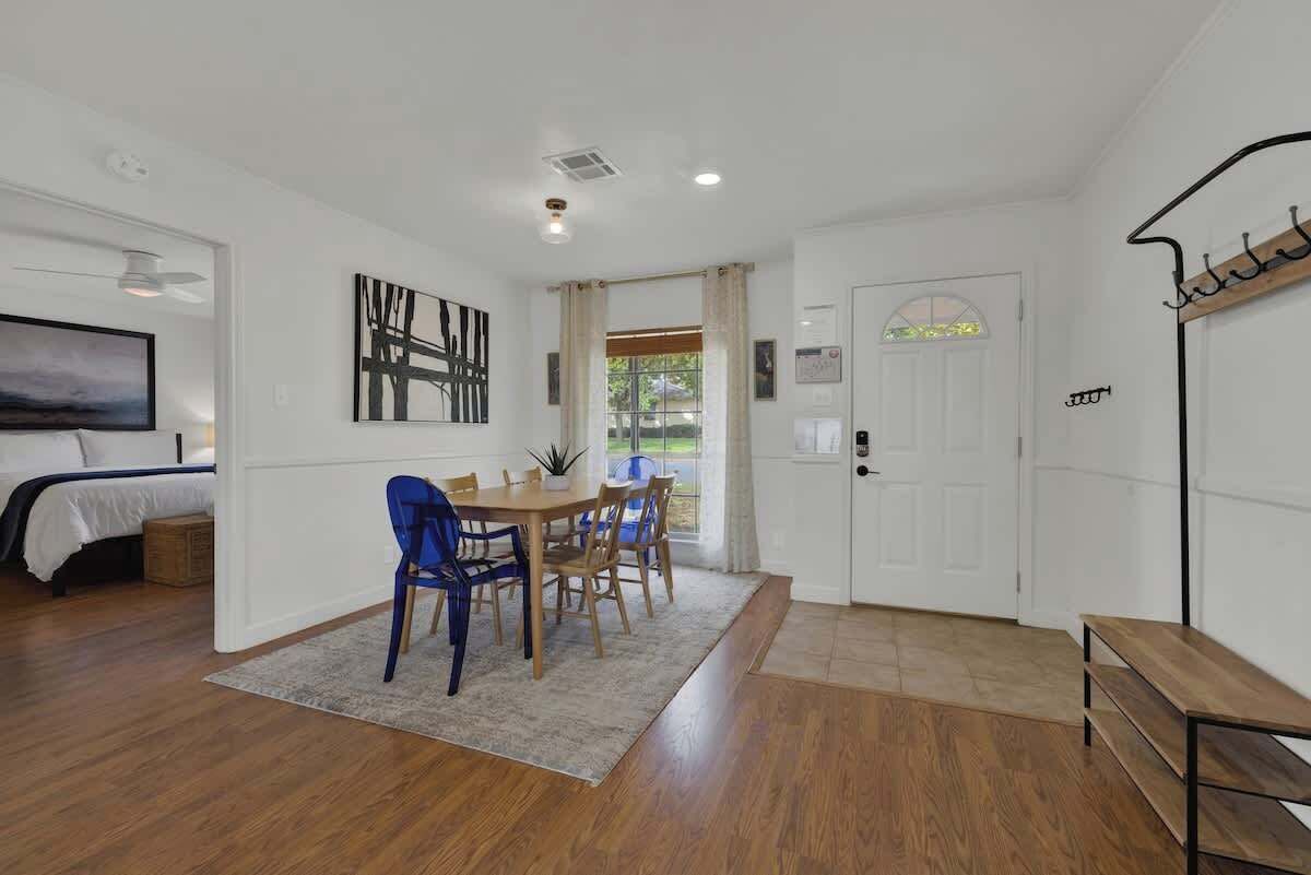 A room with a bed, a dining table with chairs, a TV, and a door with a sign.