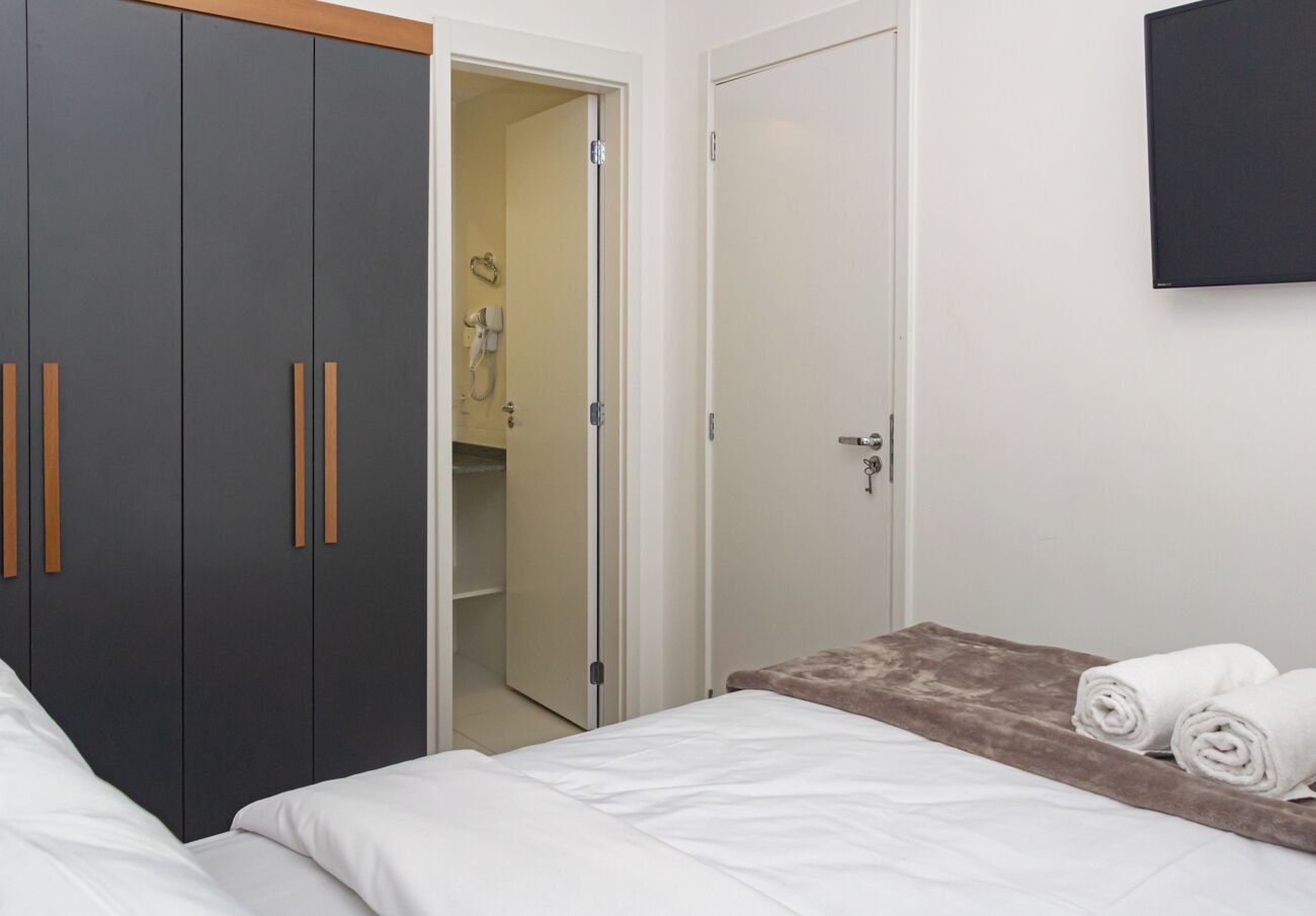 A bedroom with a bed, a wardrobe, a bathroom, and a TV on the wall.
