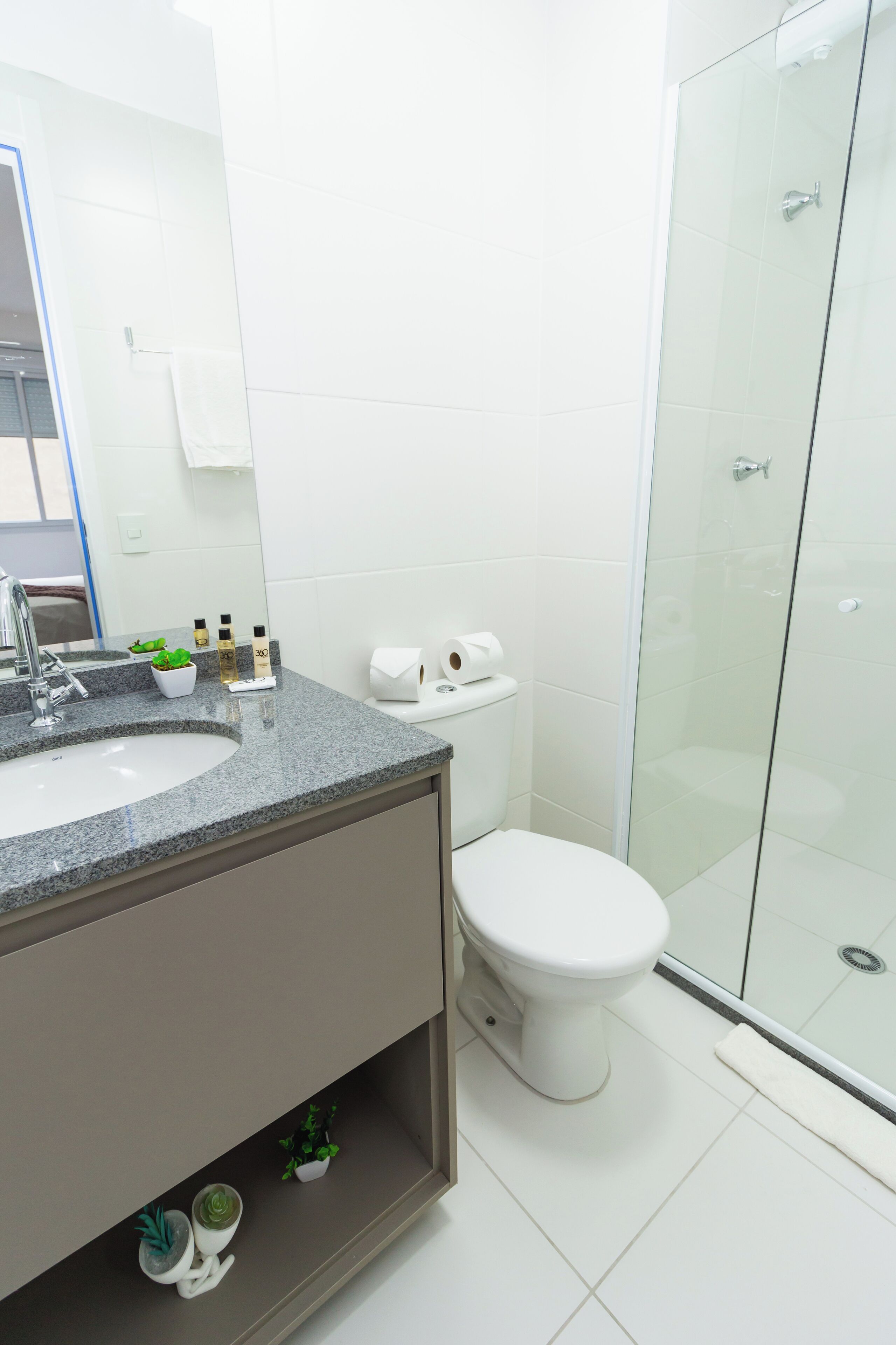 Un baño moderno con lavamanos de encimera de granito, inodoro y cabina de ducha de vidrio.