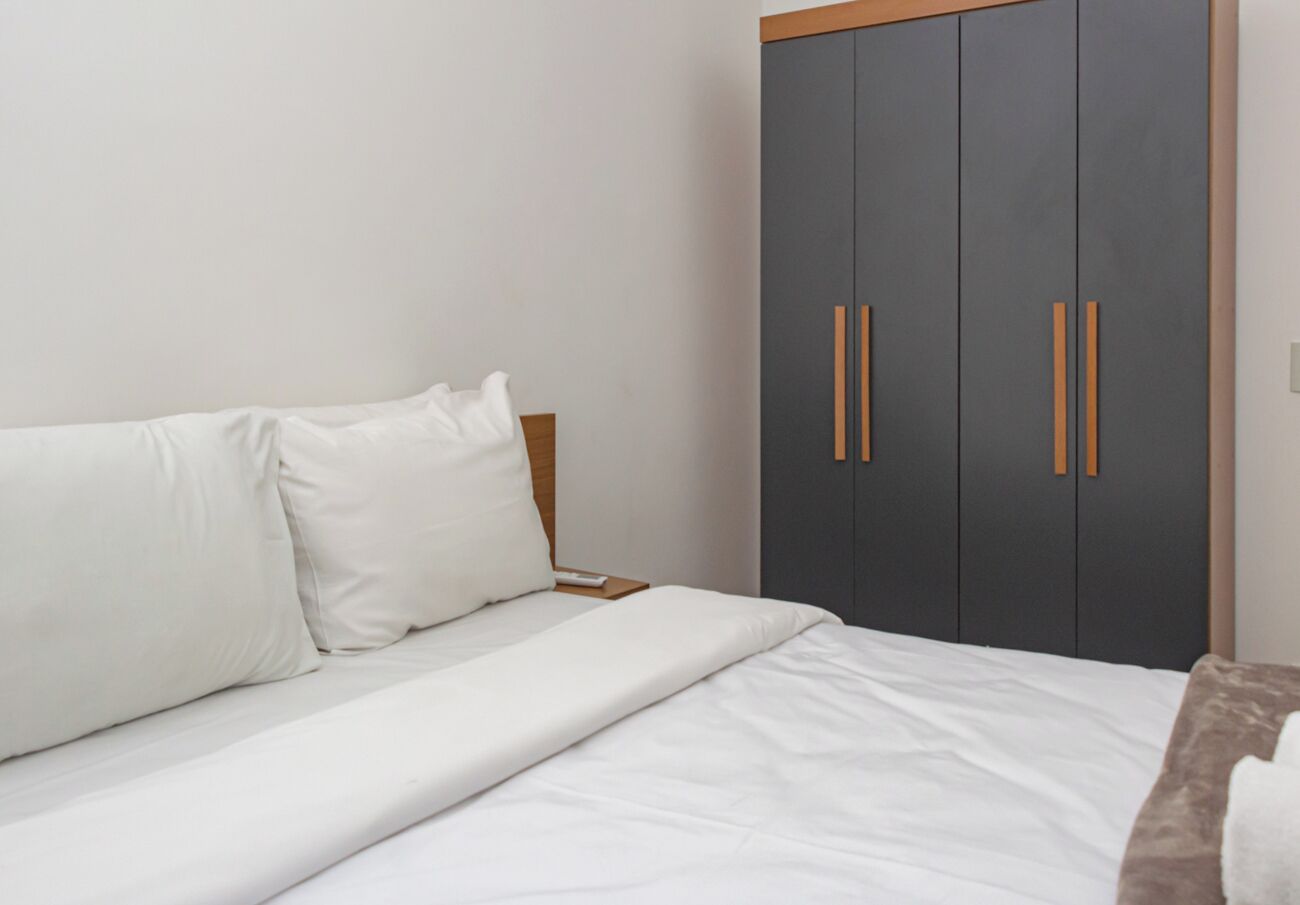 A bedroom with a bed, white bedding, a nightstand, and a wardrobe with wooden handles.