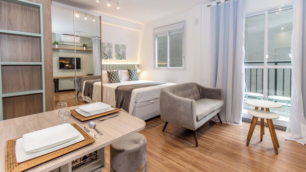 A modern hotel room with a bed, a sofa, a dining table with plates and cutlery, a small round table, and a large window with curtains. - 360 For Consolação (São Paulo)
