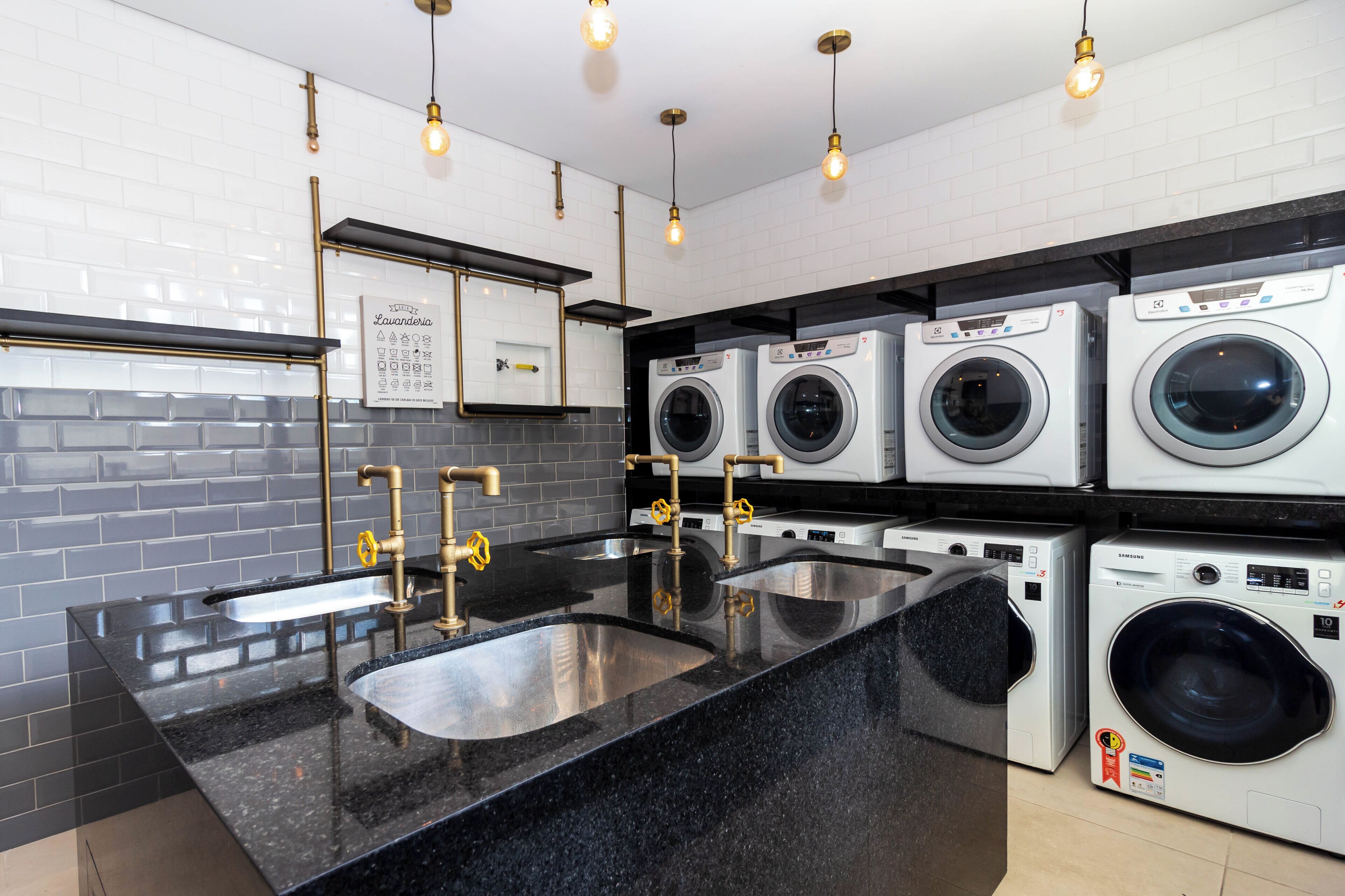 A modern laundry room with multiple washing machines, a granite countertop, and a sink with gold fixtures.