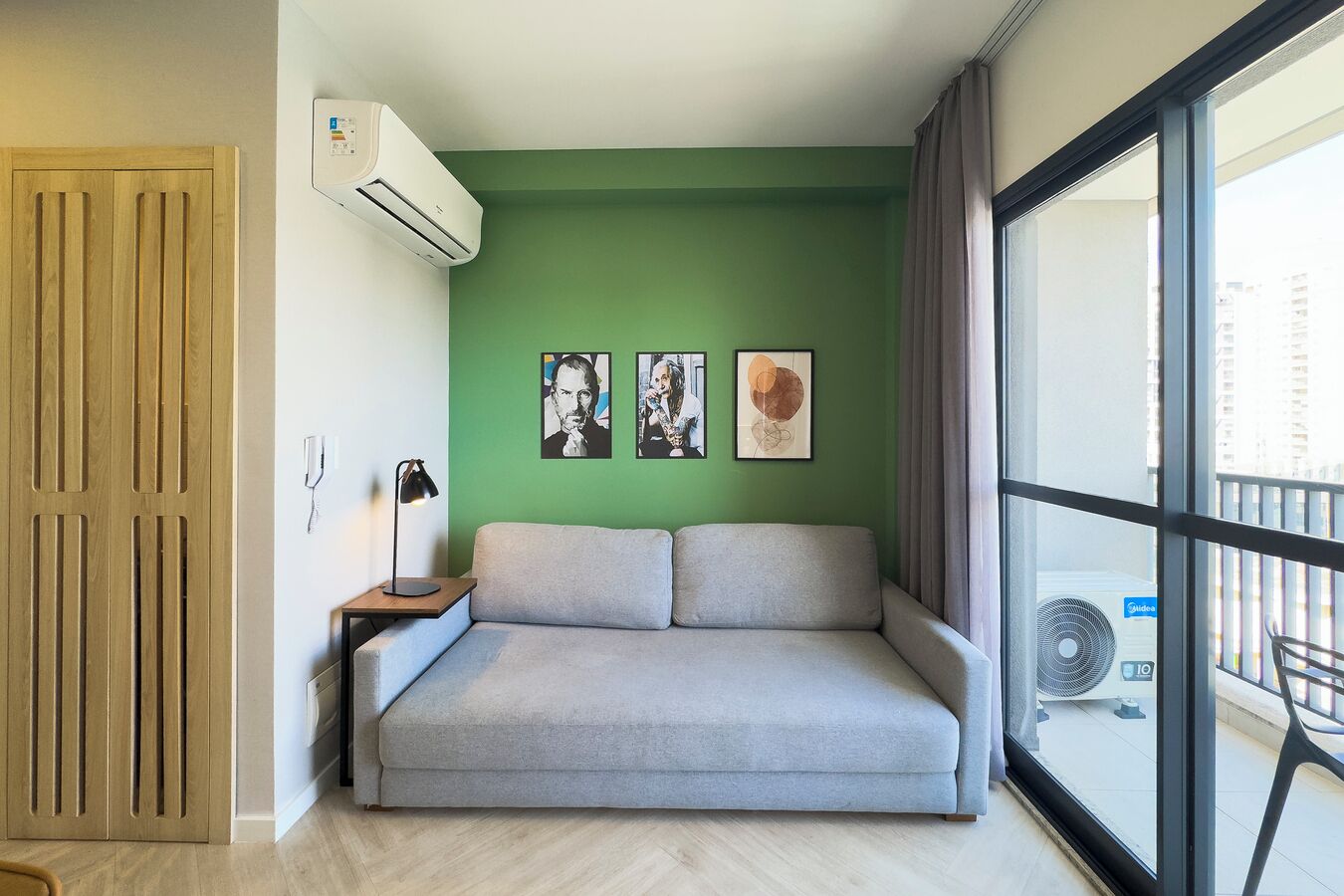 A modern living room with a grey sofa, a wooden door, and a large window with a view of buildings.