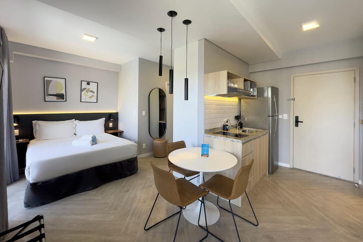 Une chambre d’hôtel moderne dotée d’un grand lit, d’une table à manger avec des chaises, d’un coin cuisine et d’une salle de bain.