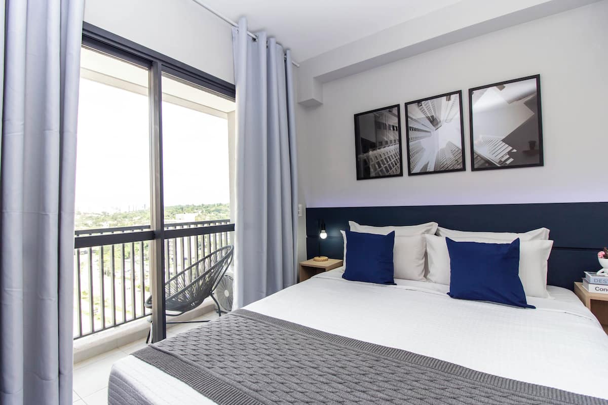 Une chambre d’hôtel avec un grand lit, un balcon avec une chaise et deux tableaux encadrés au mur.