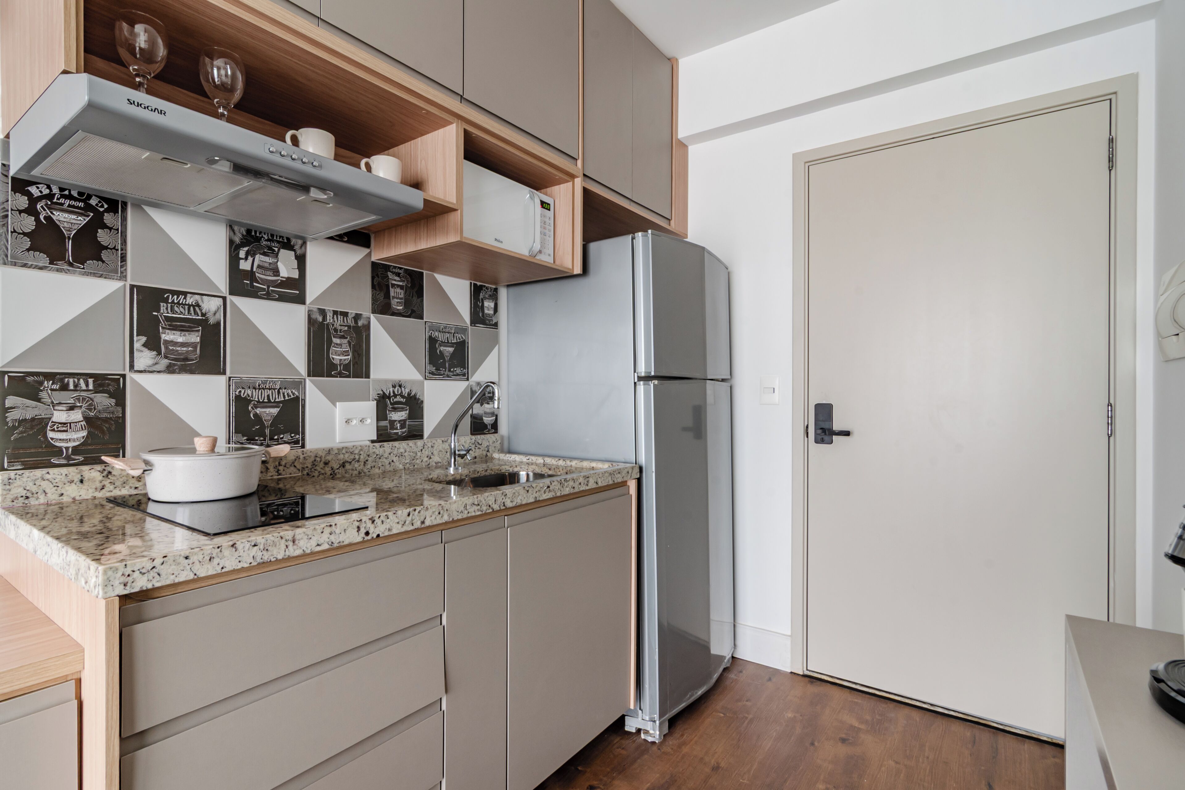 A modern kitchen with a granite countertop, stainless steel appliances, and a wooden backsplash with black and white tiles.