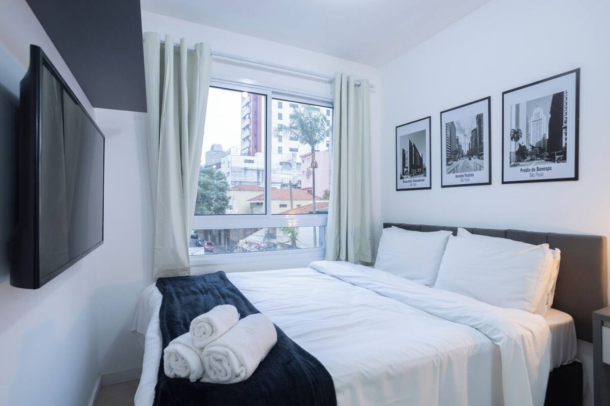Ein Hotelzimmer mit einem großen Bett, einem wandmontierten Flachbildfernseher und drei gerahmten Bildern mit Stadtansichten.