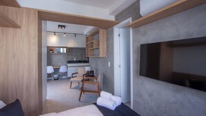 Et moderne hotelværelse med en seng, et siddeområde med stole, et lille tekøkken og et stort vindue.