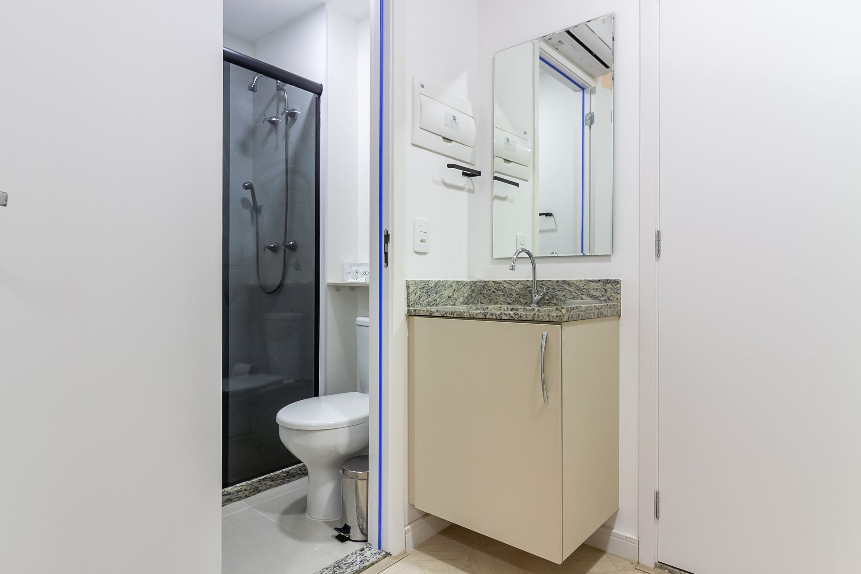A bathroom with a glass shower enclosure, a toilet, a sink with a granite countertop, and a mirror with a towel rack.