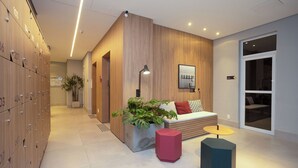 En moderne hotellobby med et træbeklædt omklædningsområde, et siddeområde med en plante og et stort vindue.