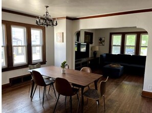 Un comedor con una mesa y sillas de madera, una araña y una cocina al fondo.