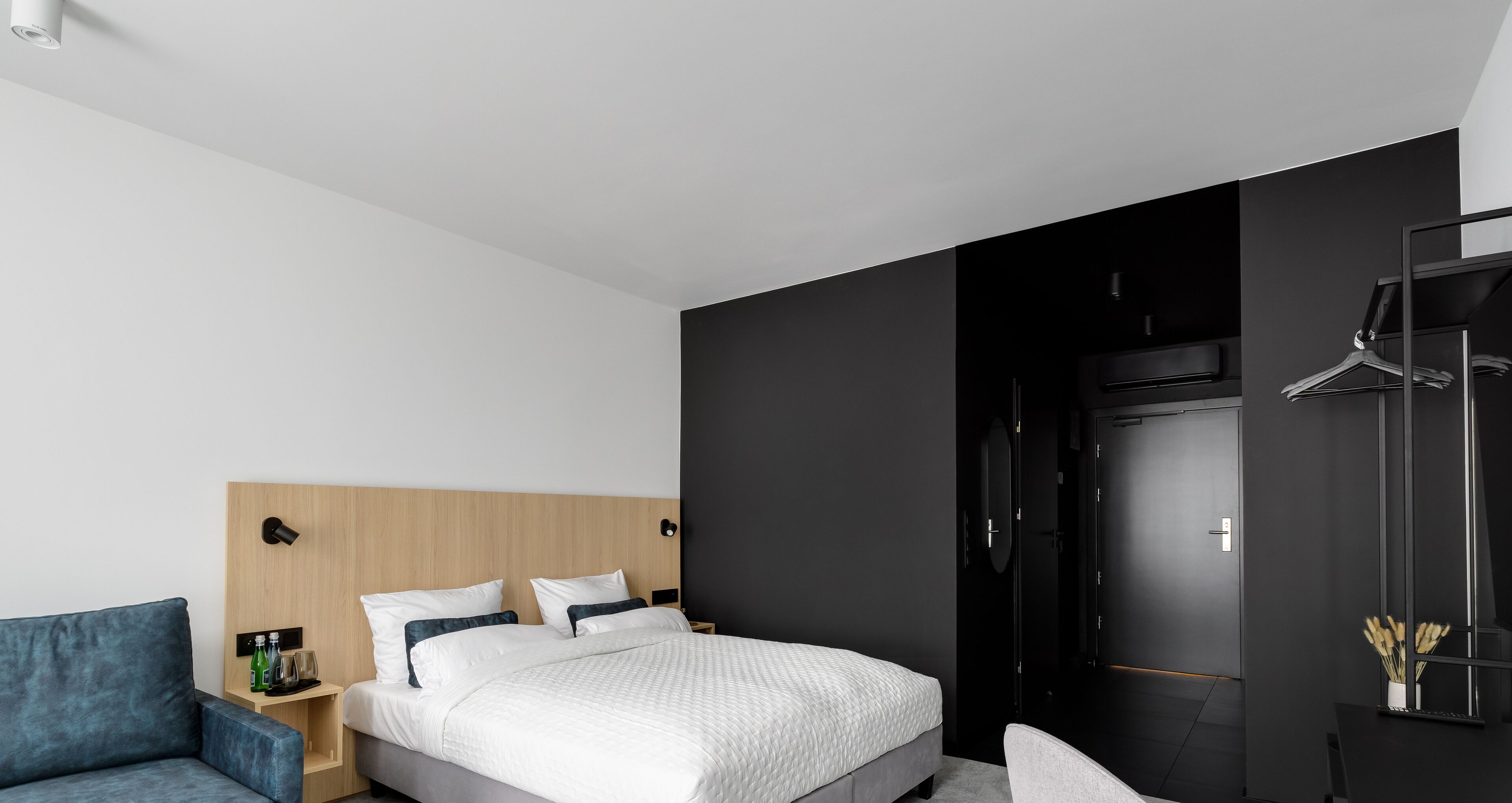 Une chambre d’hôtel moderne avec un lit, un canapé bleu, une armoire et un bureau avec une chaise.