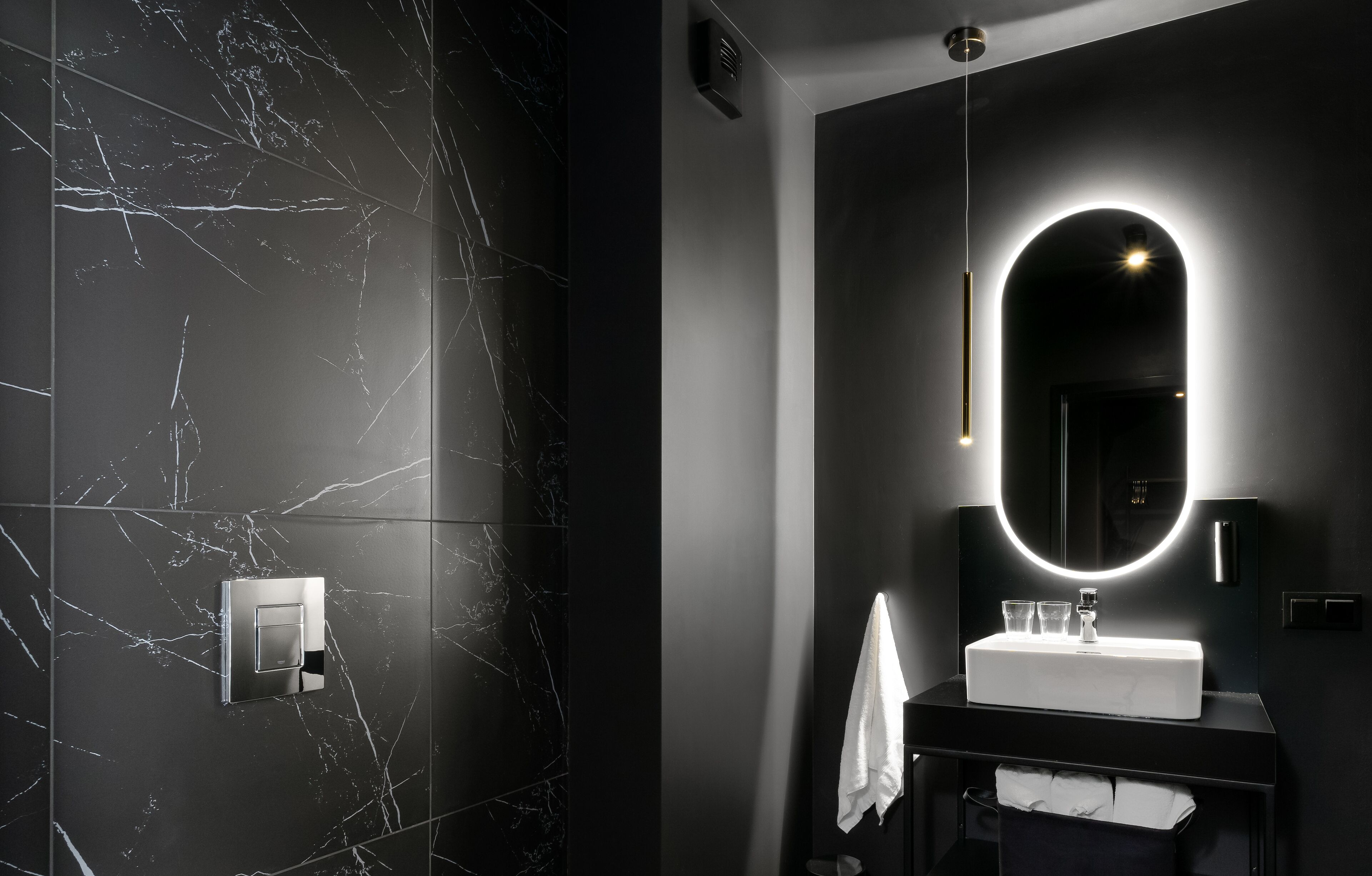 Un baño moderno con pared de mármol, un lavabo blanco y un espejo con luz.