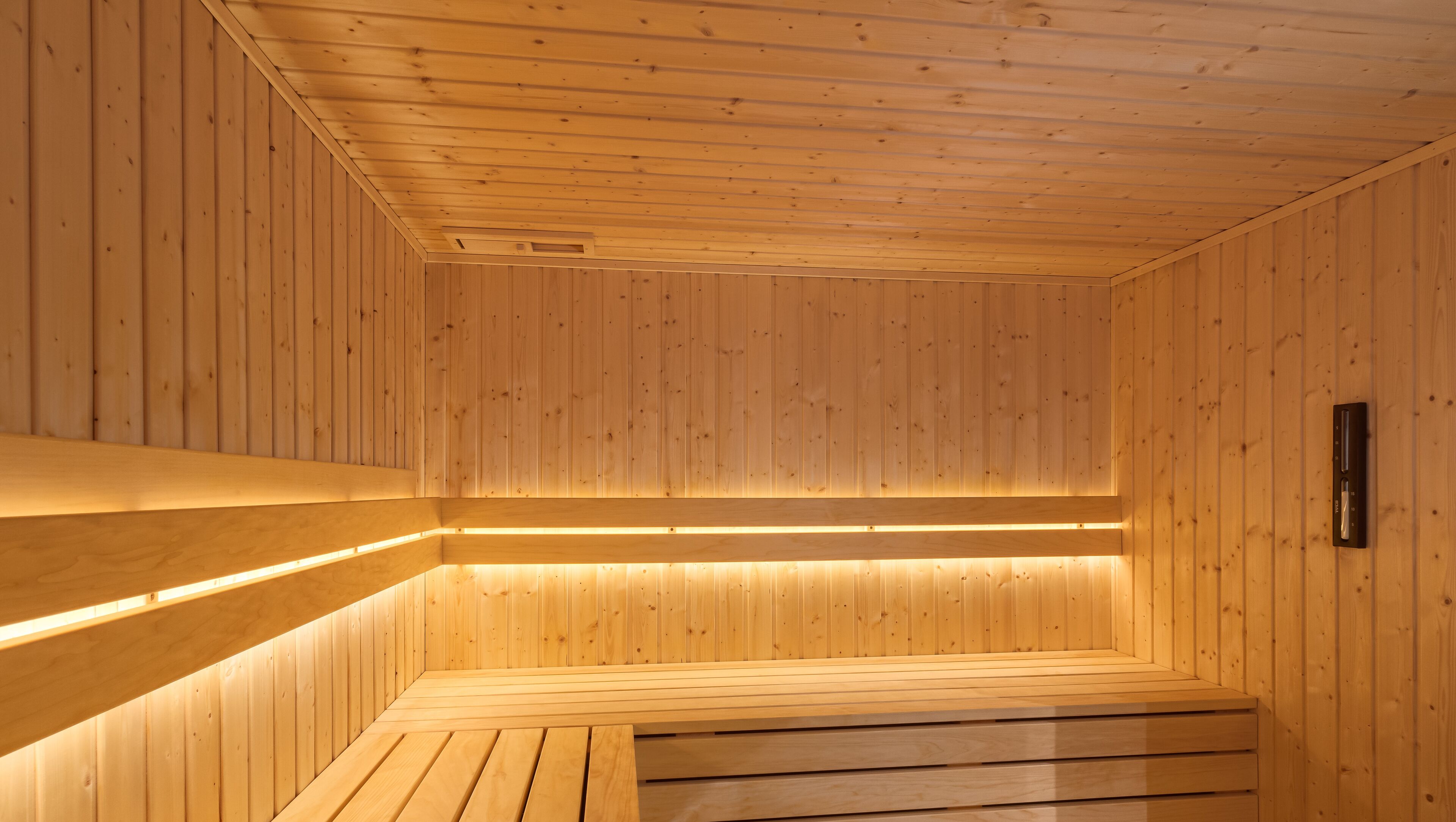 A sauna with wooden walls and benches, featuring built-in lighting along the benches.