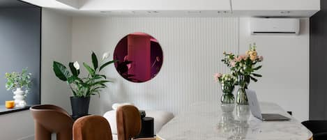 Un interior moderno con una mesa redonda de mármol, dos sillones de terciopelo marrón, una planta en maceta y un aire acondicionado de pared.