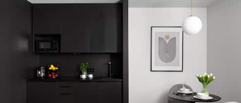 A modern kitchen with black cabinets, a microwave, and a coffee machine. There is a dining area with a table, chairs, and a vase of flowers.