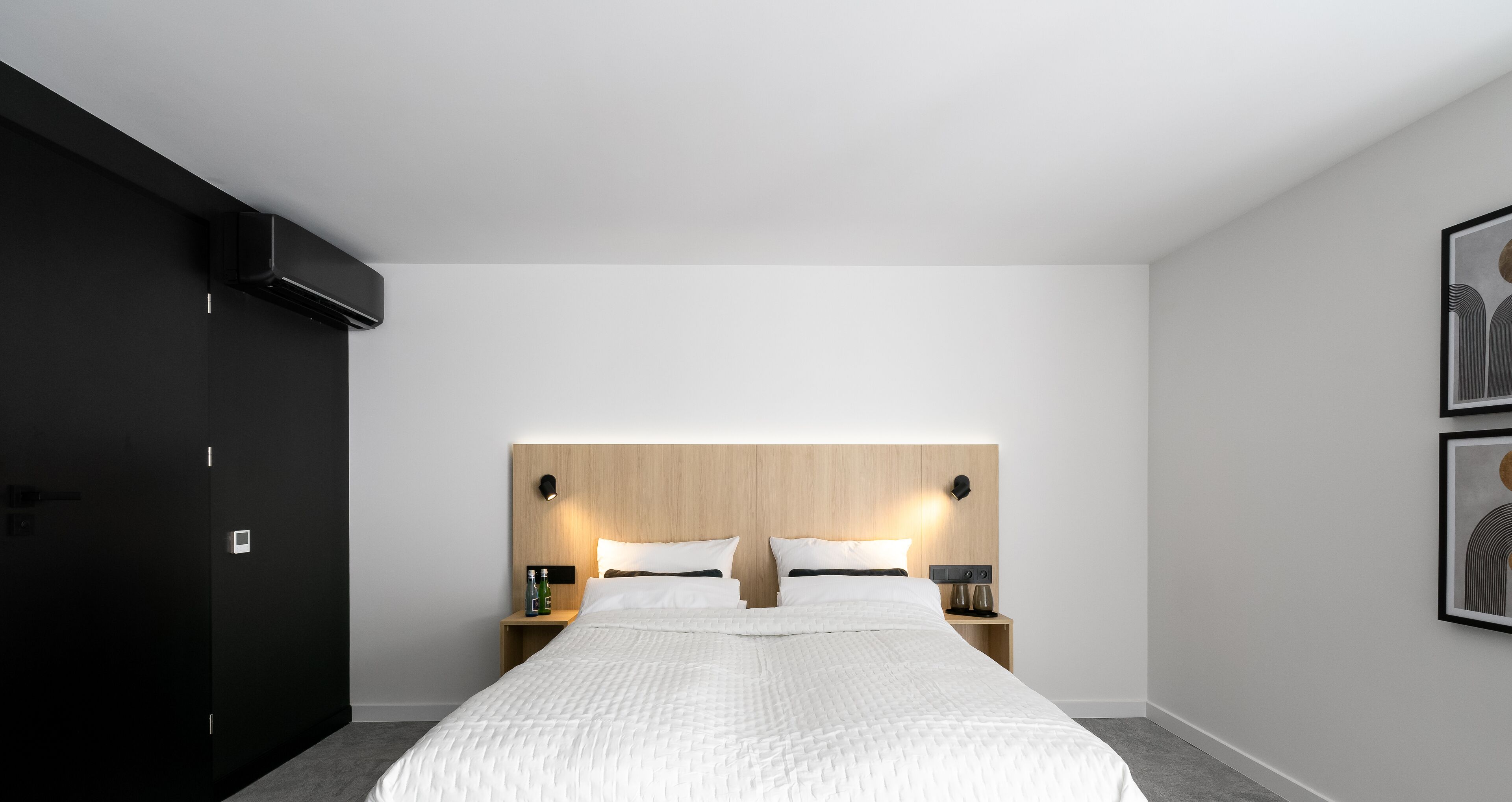 Ein modernes Hotelzimmer mit einem großen Bett, einem Holz-Kopfteil, Nachttischen mit Lampen und einem Bild an der Wand.