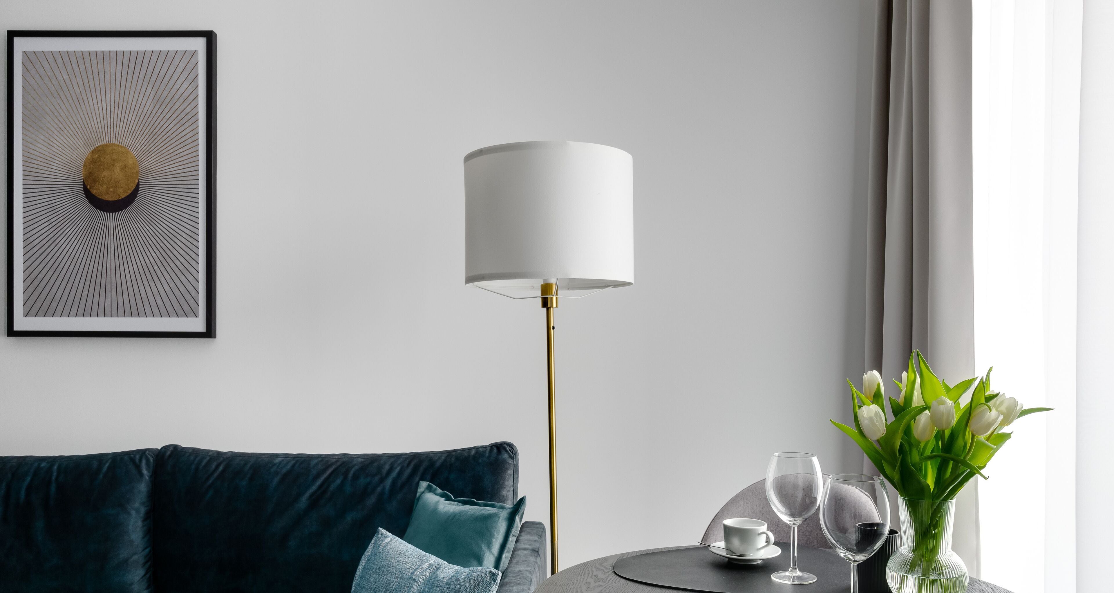 Ein modernes Wohnzimmer mit einem dunkelblauen Sofa, einem runden Tisch mit einer weißen Lampe, einem gerahmten abstrakten Kunstwerk und einer Vase mit weißen Blumen.