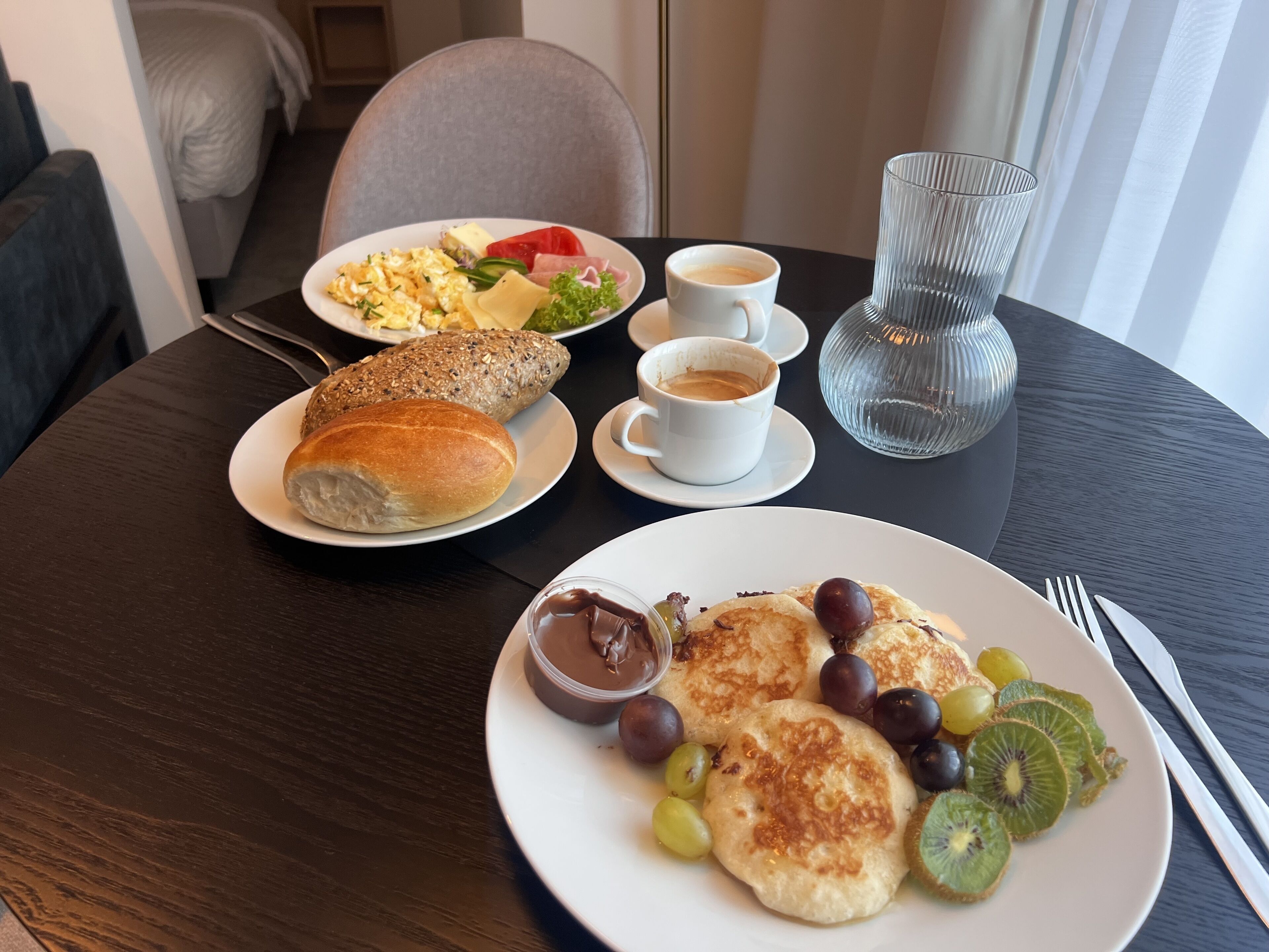 A breakfast setting with a plate of eggs, bread, and fruit, and two cups of coffee on a table.