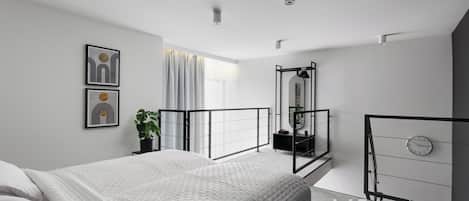 Un dormitorio moderno con una cama grande, una mesita de noche con una planta, un espejo y un reloj en la pared.