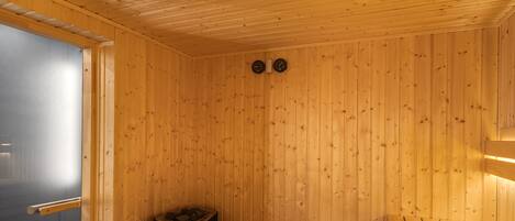 A sauna room with wooden walls, a bench, and two wall-mounted clocks.