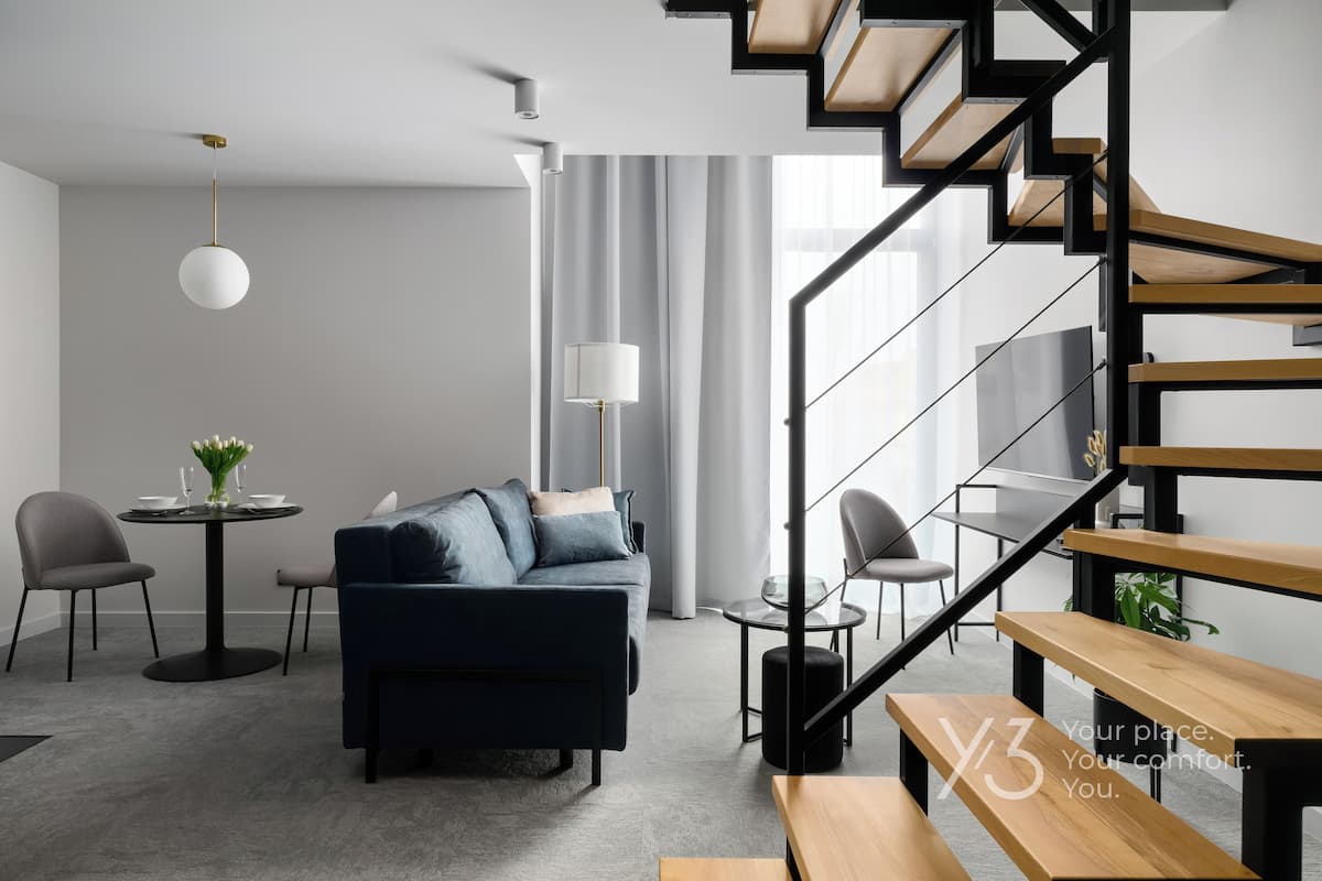 A modern living room with a sofa, coffee table, and chairs, a staircase, and a dining area with a table and chairs.